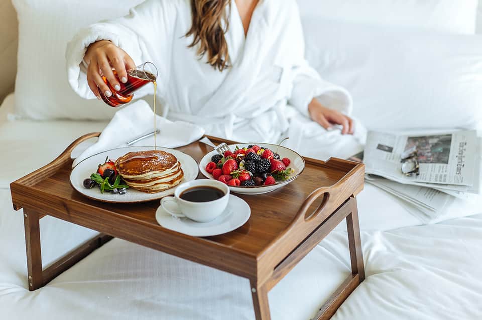 Woman enjoying breakfast in bed with pancakes, berries, and coffee while reading