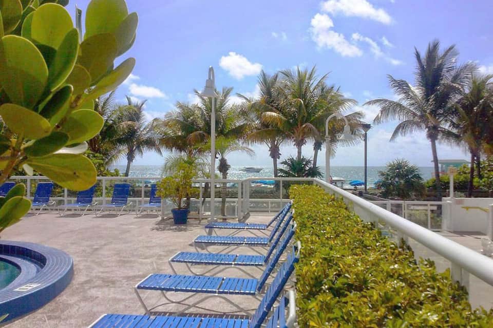 Oceanfront terrace with palm trees, blue lounge chairs, and sea views with white umbrella