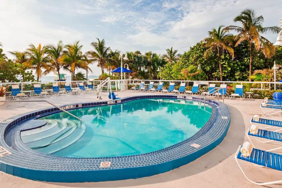 Curved resort swimming pool with turquoise water, blue loungers, and palm trees