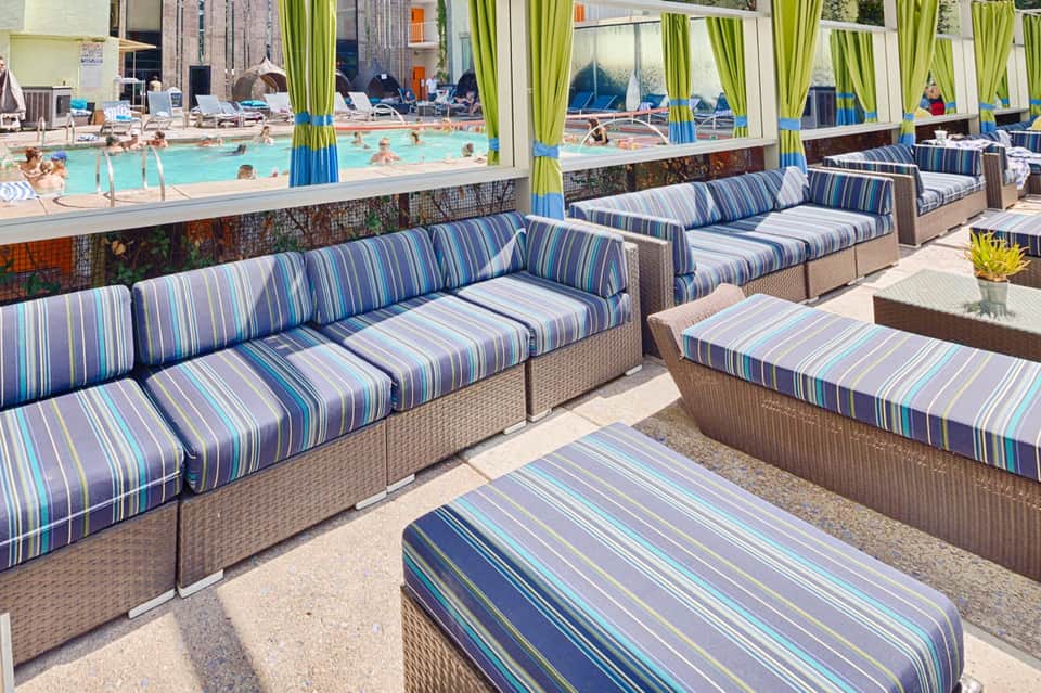 Striped lounge chairs and sofas on pool deck overlooking bright blue swimming pool with green curtains