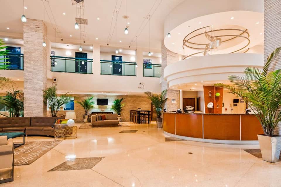 Modern hotel lobby with multi-level atrium, circular chandelier, wood reception desk, and plants