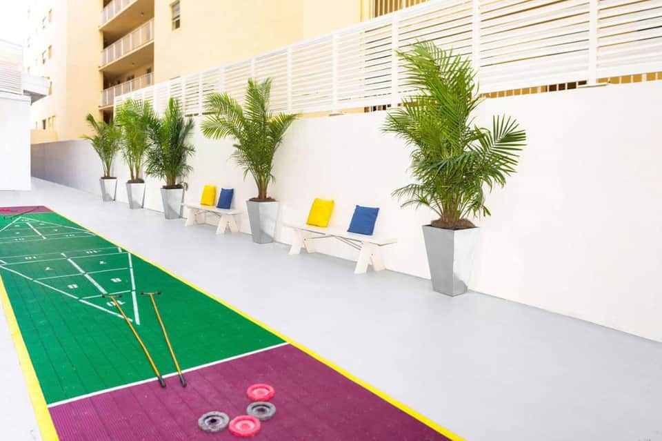 Modern courtyard with green sports court, palm planters, and yellow and blue lounge chairs