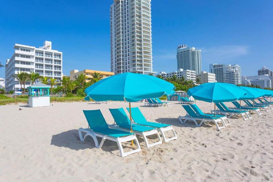 Miami beach with bright turquoise umbrellas and loungers facing high-rise hotels