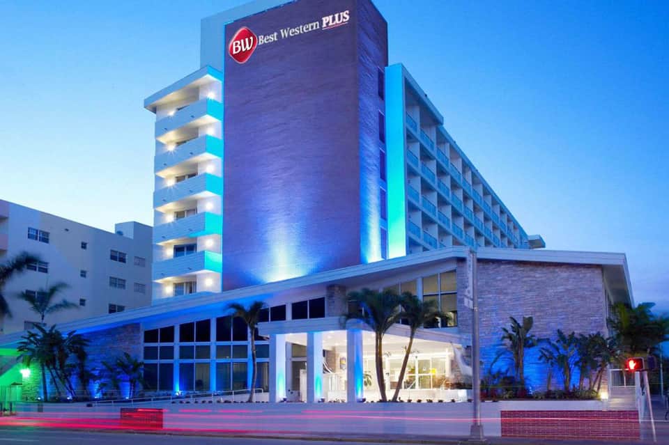 Best Western Plus hotel exterior at night with blue and green neon lighting and palm trees