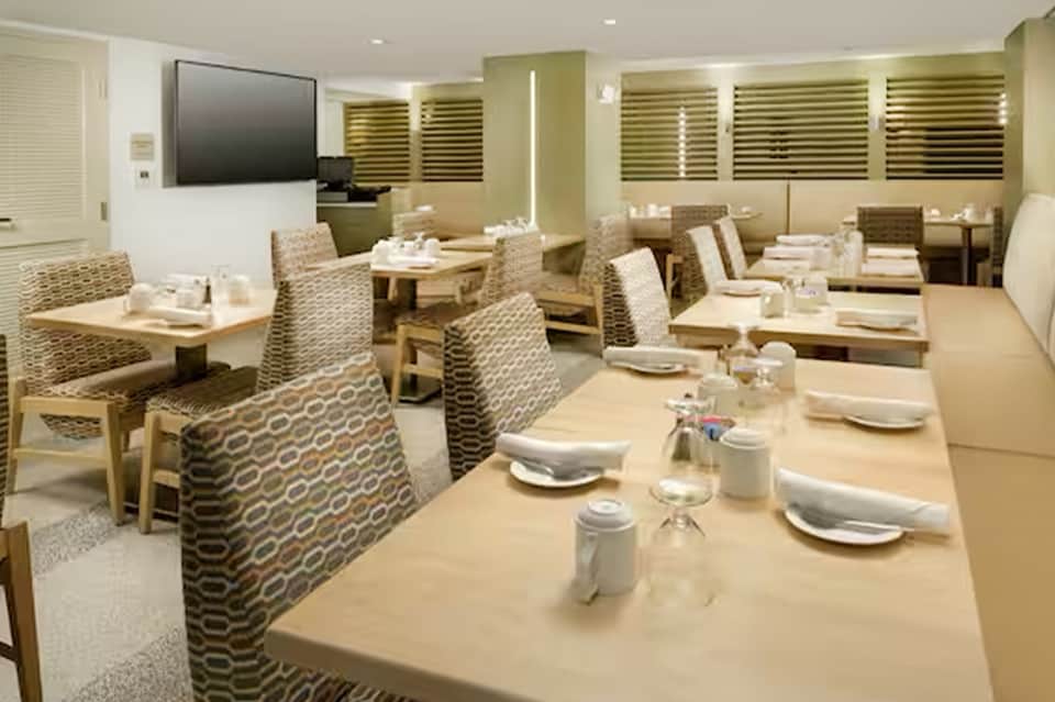 Formal dining room with patterned chairs, wooden tables, place settings, TV screen, and green accents