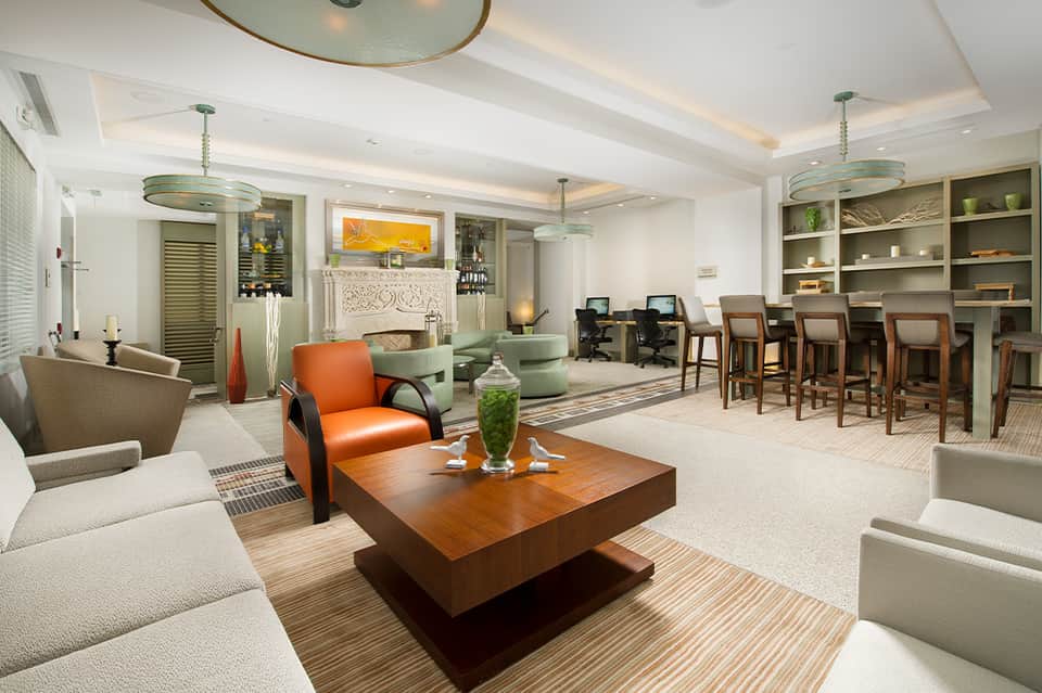 Elegant hotel lobby with fireplace, orange accent chair, green pendant lights, and dining area