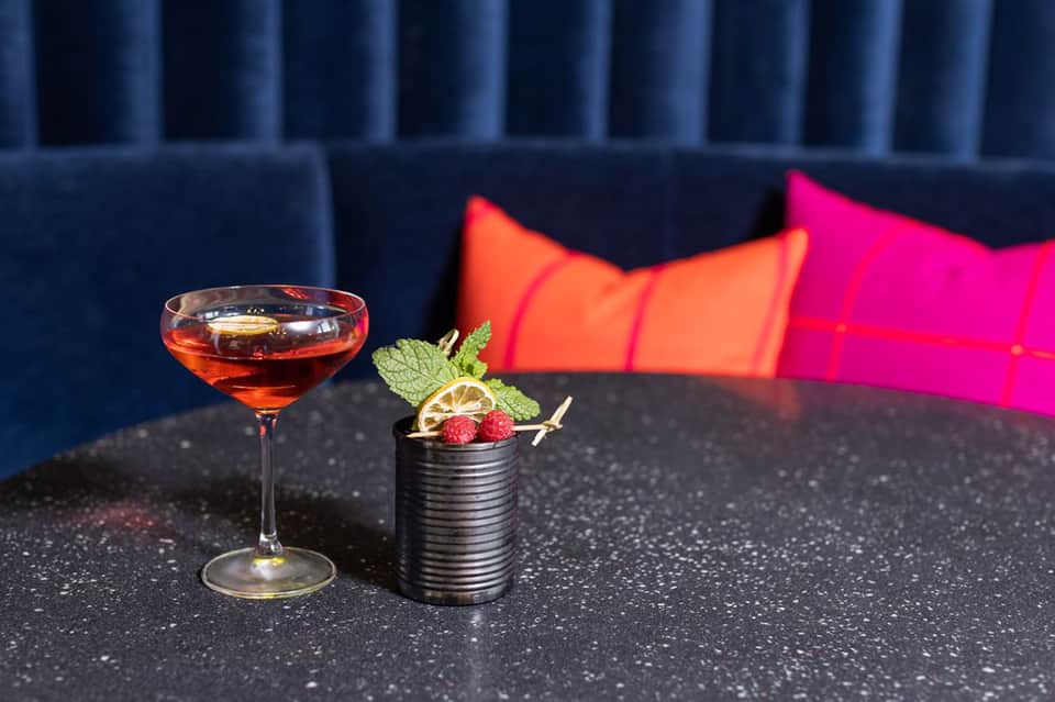 Signature cocktail on dark bar counter with colorful cushioned seating in background