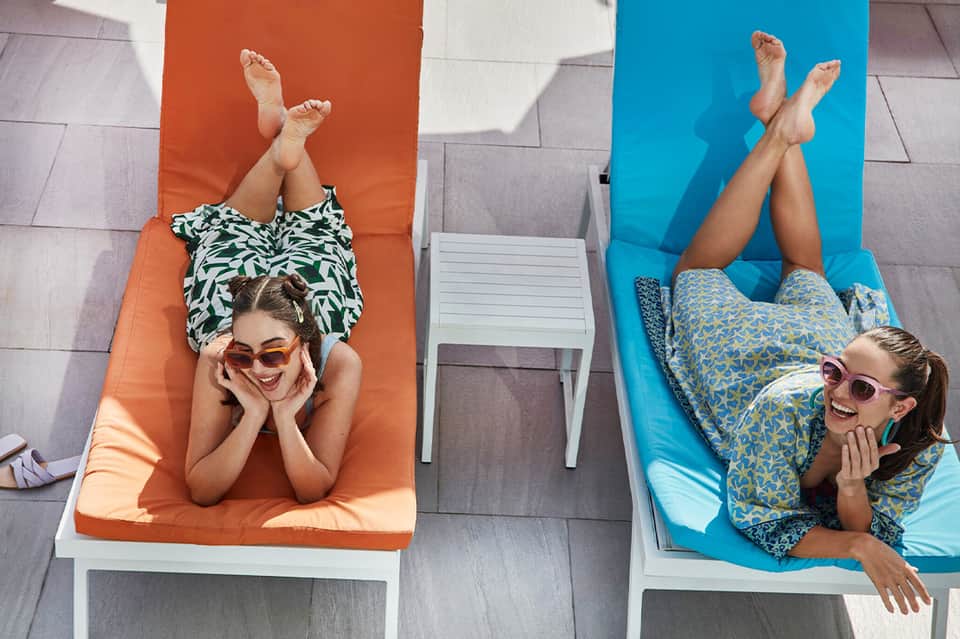 Two women relaxing on colorful lounge chairs by the pool from overhead view