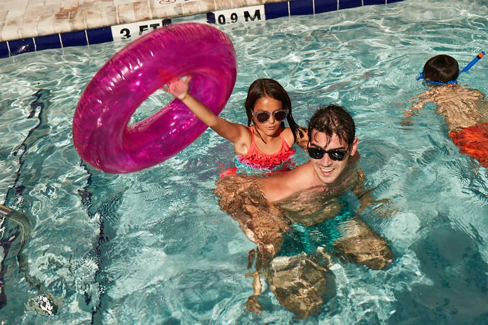 Family swimming in resort pool with pink inflatable ring and colorful pool floats
