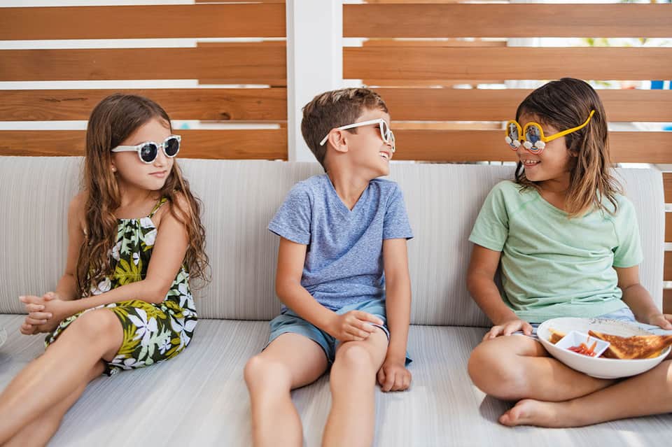 Three children in casual clothes sitting on a lounge chair with snacks