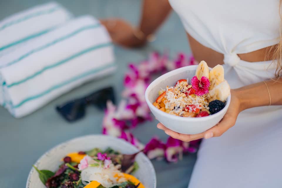 Woman holding a colorful acai bowl with granola and fresh fruit by the pool