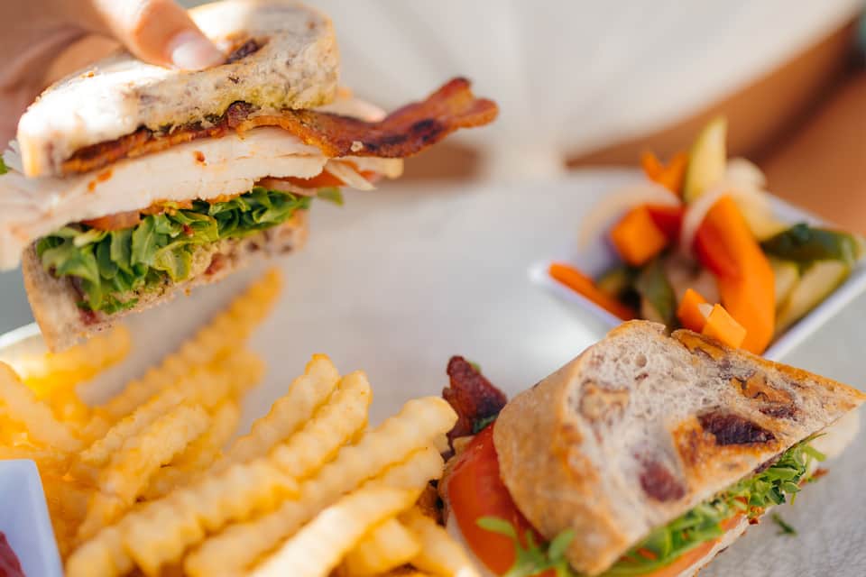 Close-up of gourmet sandwich with bacon, lettuce, and tomato served with crispy fries and fresh vegetable sides.