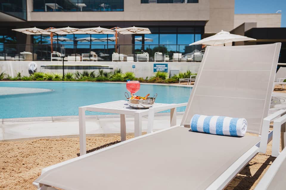 Lounge chair by resort pool with cocktail and snacks on side table