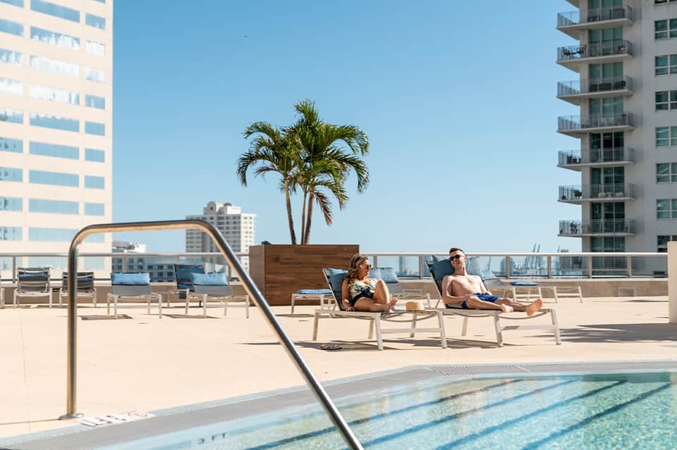 Rooftop pool deck with lounge chairs, palm tree, and high-rise apartment buildings