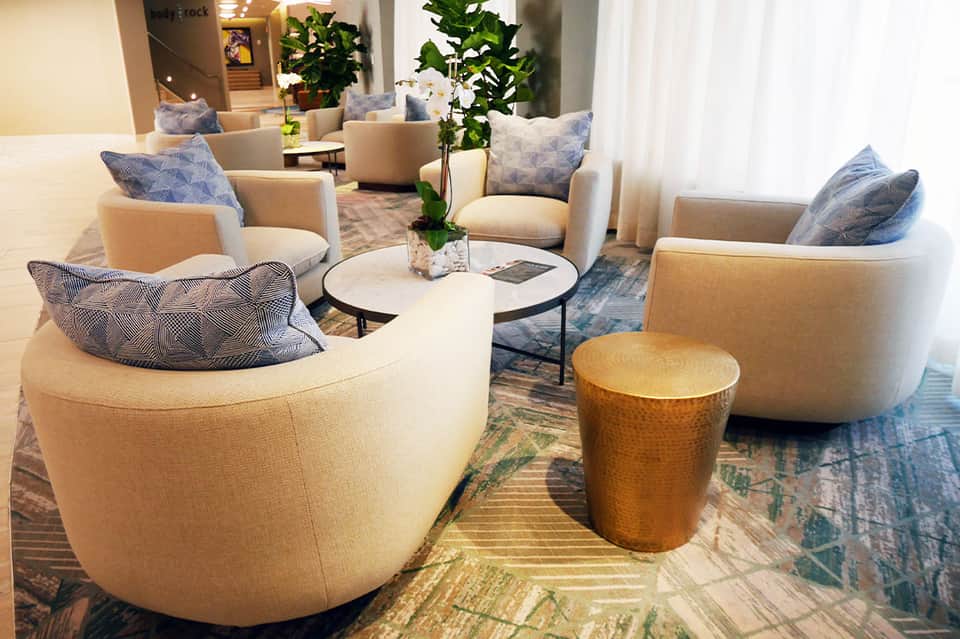 Contemporary hotel lobby lounge with cream-colored curved chairs, blue patterned pillows, and plants