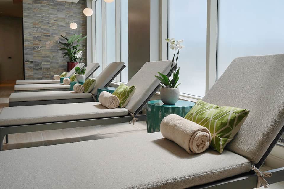 Spa relaxation area with multiple cushioned loungers, towel rolls, and ocean view windows