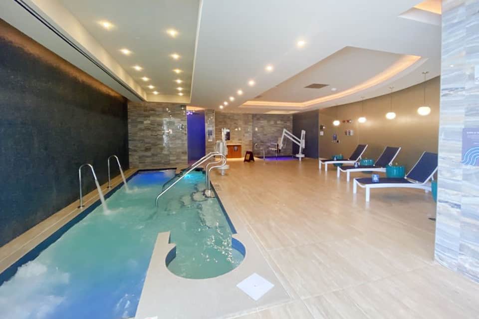 Indoor spa area with turquoise lap pool, lounge chairs, and modern stone and wood finishes