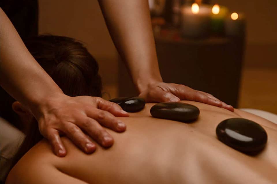 Spa therapist performing hot stone treatment on client's back in candlelit room