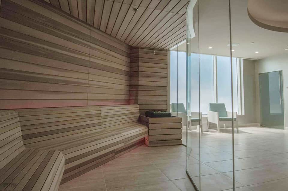 Sauna interior with wooden benches, glass door, and ocean view window overlooking terrace