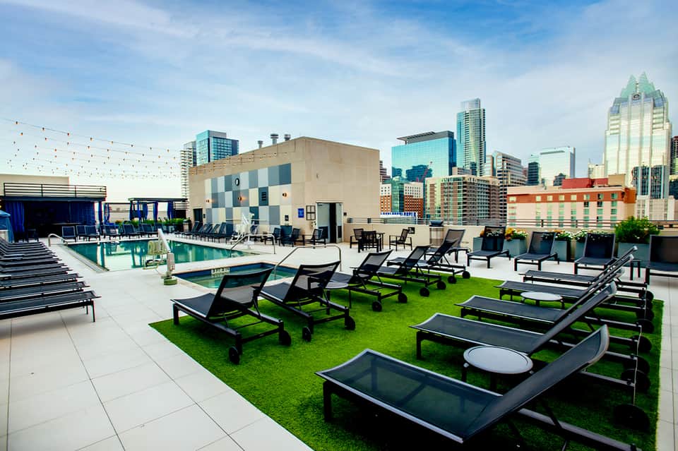 Rooftop pool deck with lounge chairs, cornhole games, and city skyline backdrop