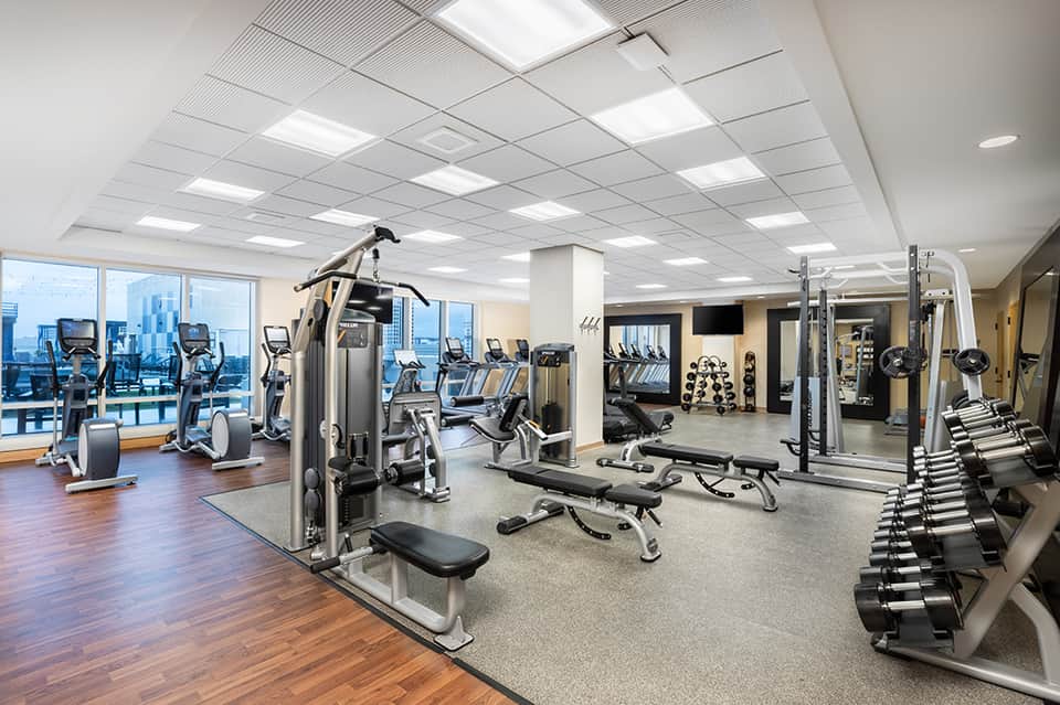 Modern fitness center with cardio equipment, dumbbells, and floor-to-ceiling windows with city views