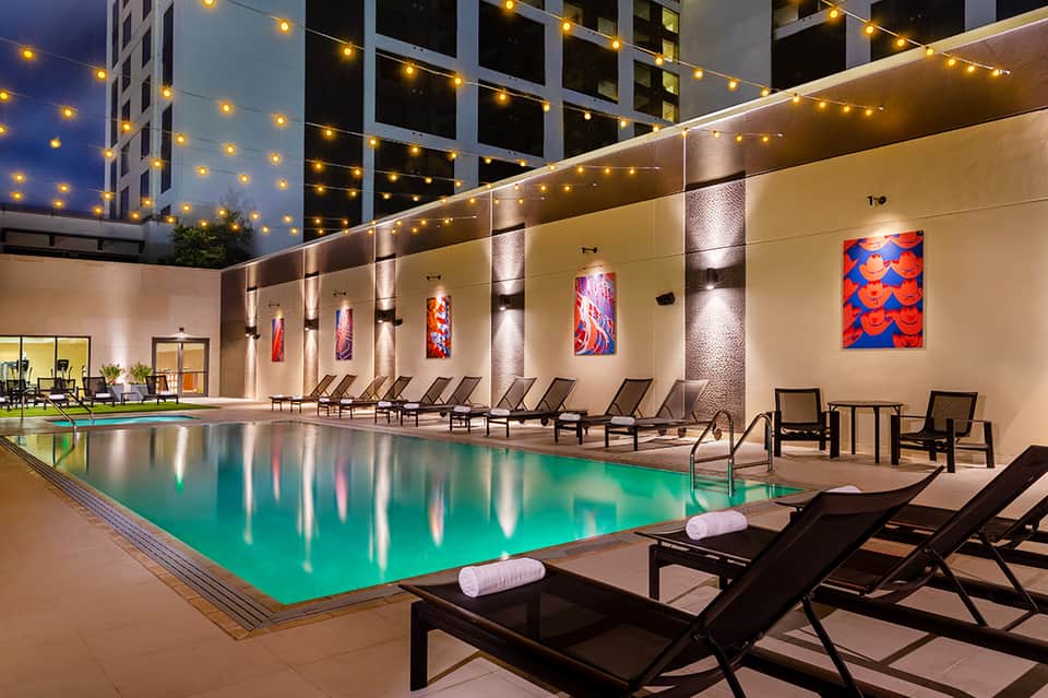 Illuminated resort pool at night with lounge chairs and modern architecture