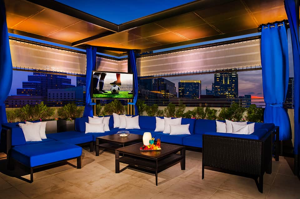 Modern rooftop lounge with blue seating, fire pit, and cityscape views at twilight