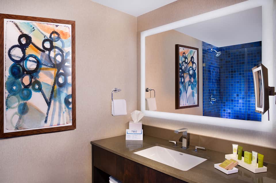 Bathroom vanity with blue tile wall, artistic framed artwork, and bright illuminated mirror