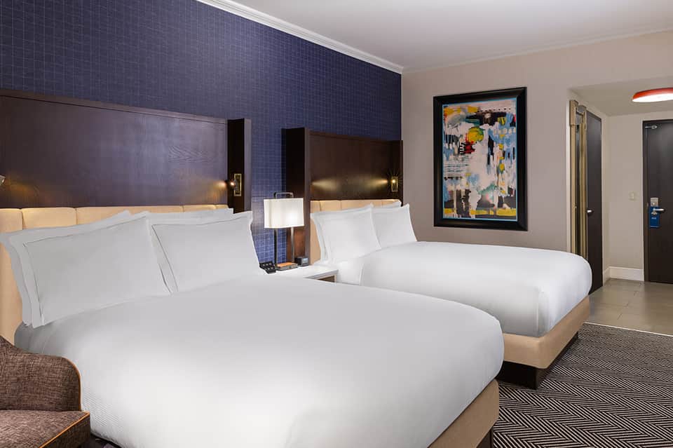 Modern hotel room with two queen beds, blue accent wall, and contemporary decor