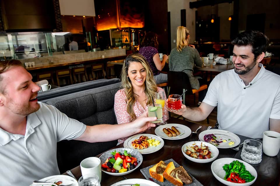 Three guests dining together with small plates and colorful beverages in modern restaurant