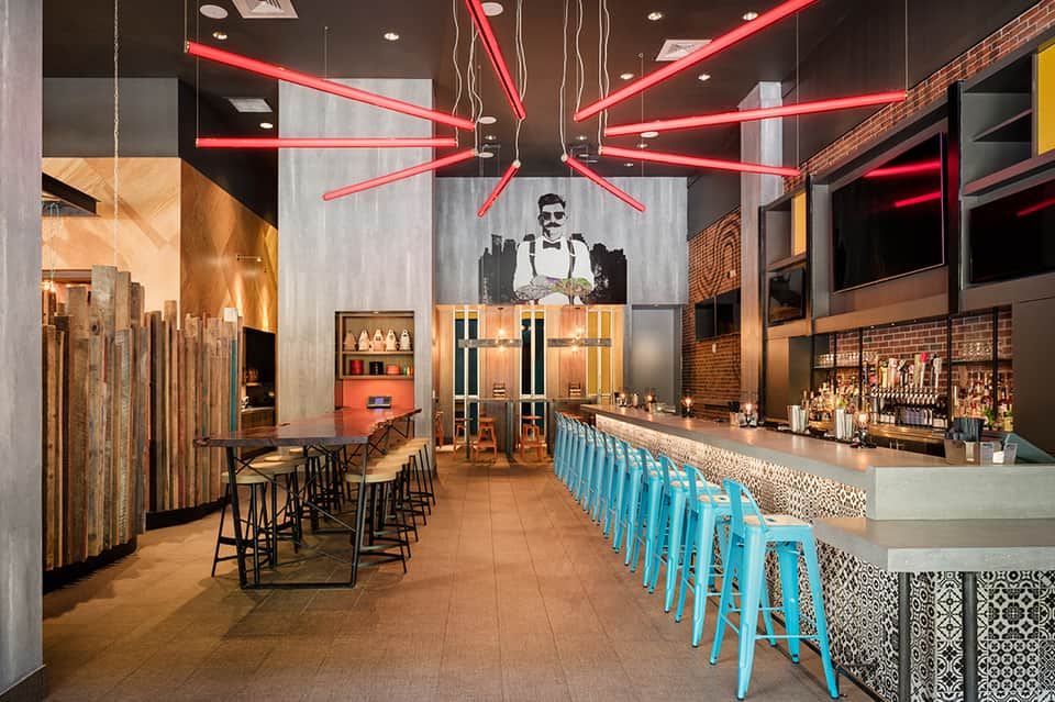 Contemporary bar with red neon lighting, exposed brick, and turquoise bar stools