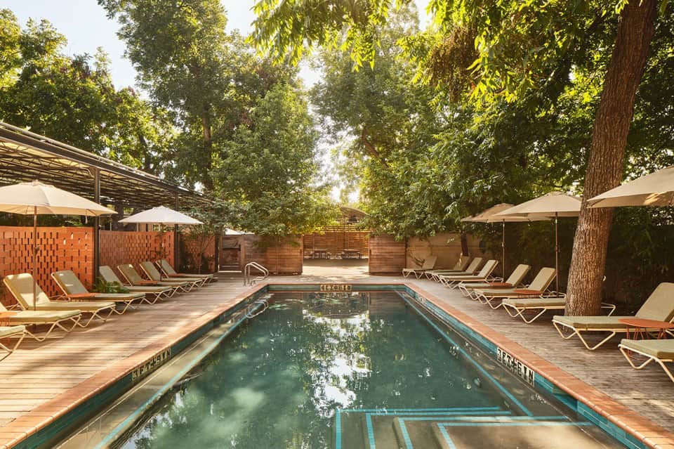 Rectangular lap pool surrounded by lounge chairs and umbrellas under mature trees