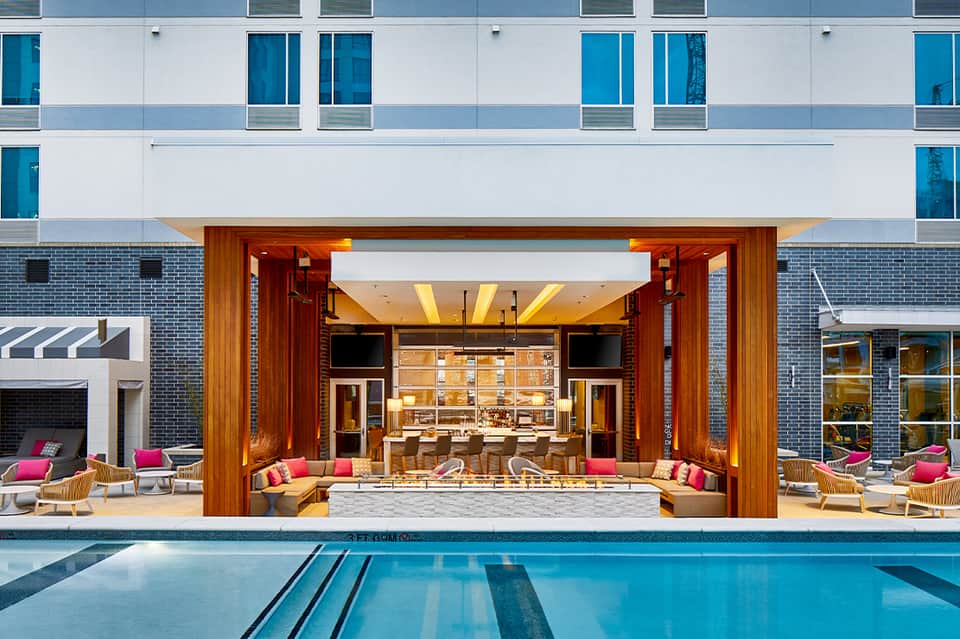 Modern hotel exterior with heated lap pool, wooden deck, and indoor lounge visible through glass doors