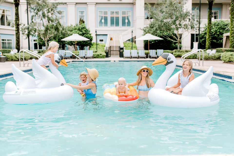 Family enjoying pool with giant swan floats and lounge chairs on white deck