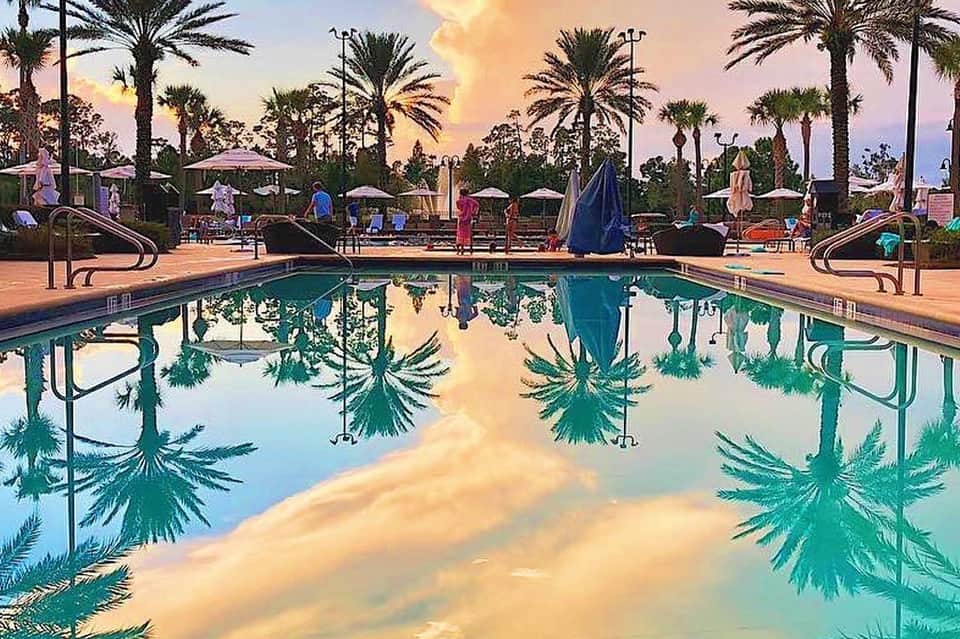 Resort pool at sunset with palm trees, umbrellas, and playground area