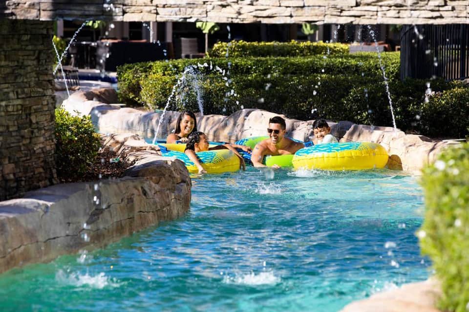 Family relaxing in resort pool with colorful floats and fountains