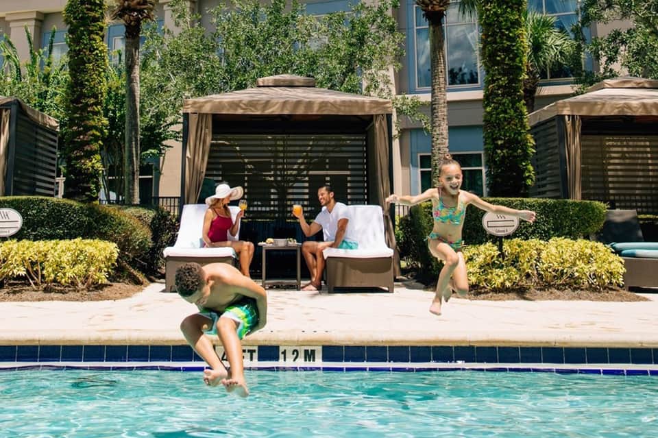 Family enjoying resort pool with cabanas, lounge chairs, and lush landscaping