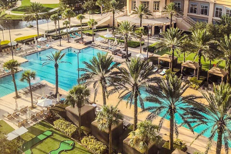 Aerial view of resort with turquoise swimming pools, palm trees, lounge chairs, and manicured grounds