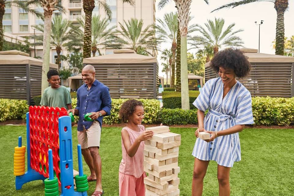 Family playing games on resort lawn with palm trees and buildings in background