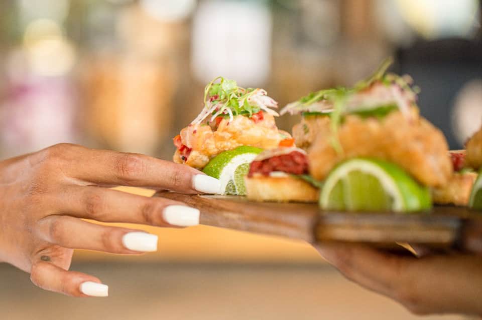 Chef presenting appetizers with lime garnish and microgreens on wooden board