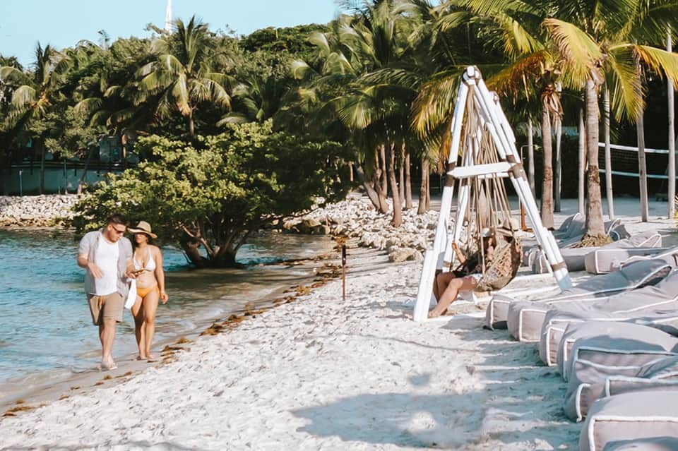 Couple walking along private beach with palm trees and white lounge chairs
