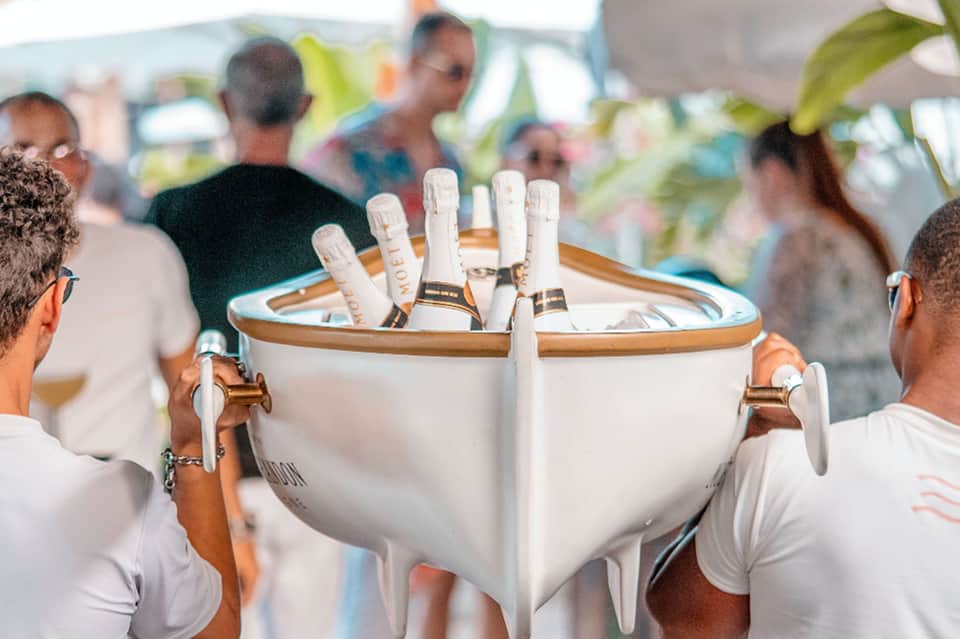 Champagne bottle bucket at outdoor event with attendees in white attire celebrating