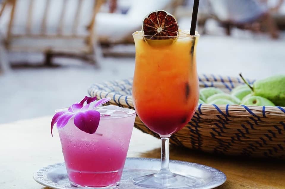 Two tropical cocktails on a table with orchid flower and ocean view behind
