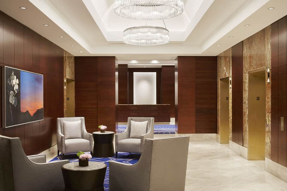 Luxury hotel elevator lobby with wood paneling, elegant seating, and crystal chandeliers