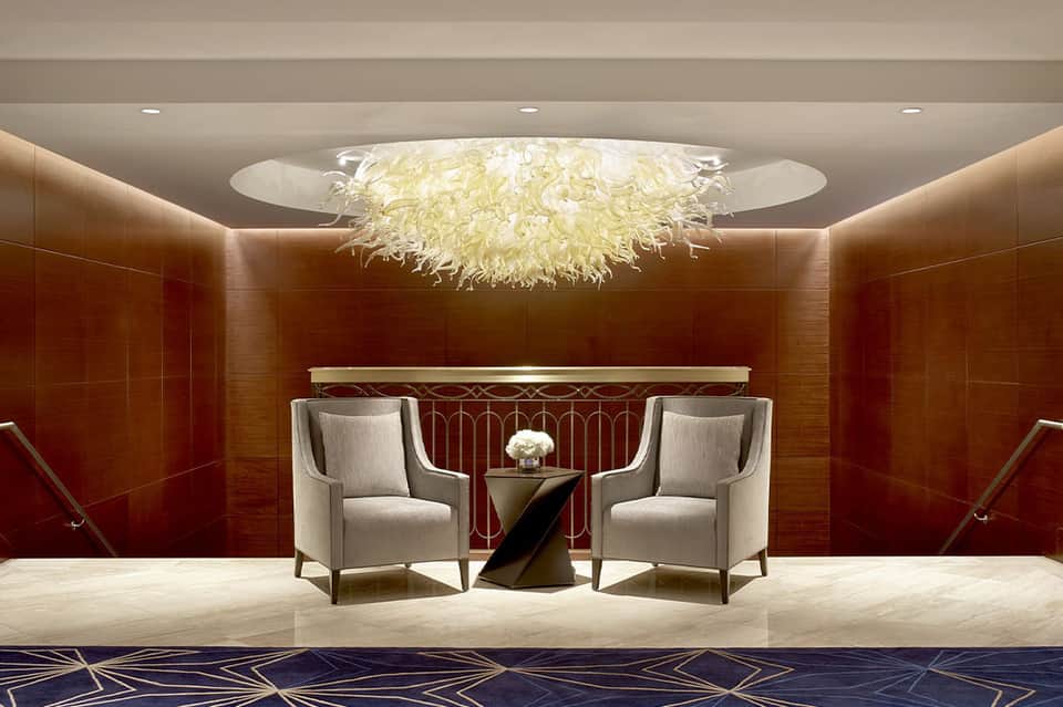 Modern hotel lobby with sophisticated seating area, feathered ceiling fixture, and warm lighting