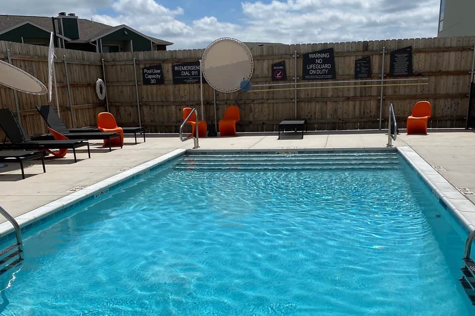 Residential pool with turquoise water, orange lounge chairs, and wooden fence