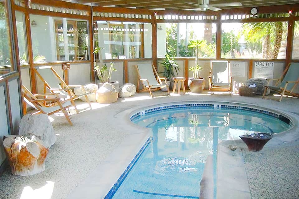 Indoor heated pool with lane dividers, wooden chairs, and palm plants visible