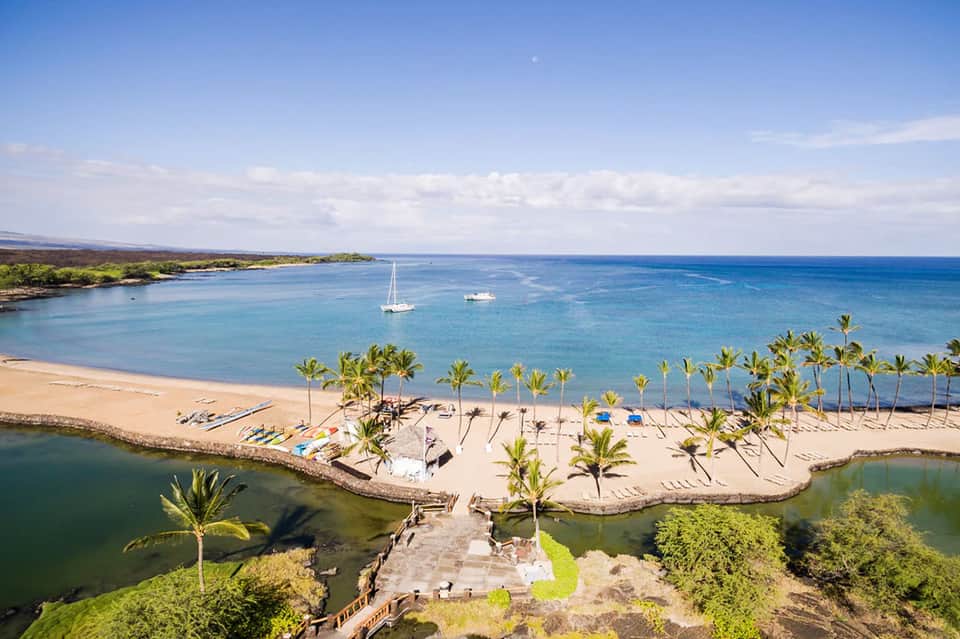Aerial beach cove with white sand, palm trees, boats, and turquoise water