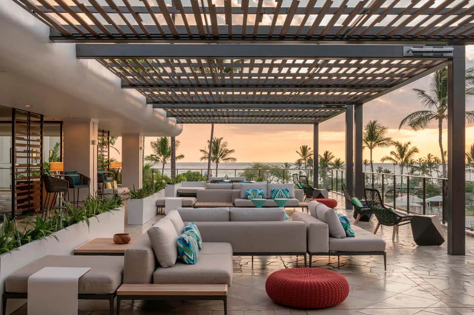 Modern beachfront terrace with gray seating, pergola, ocean and palm trees at sunset
