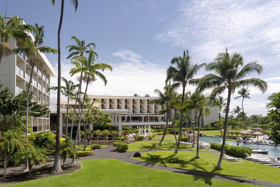 Modern resort grounds with palm trees, manicured lawn, river feature, and contemporary architecture